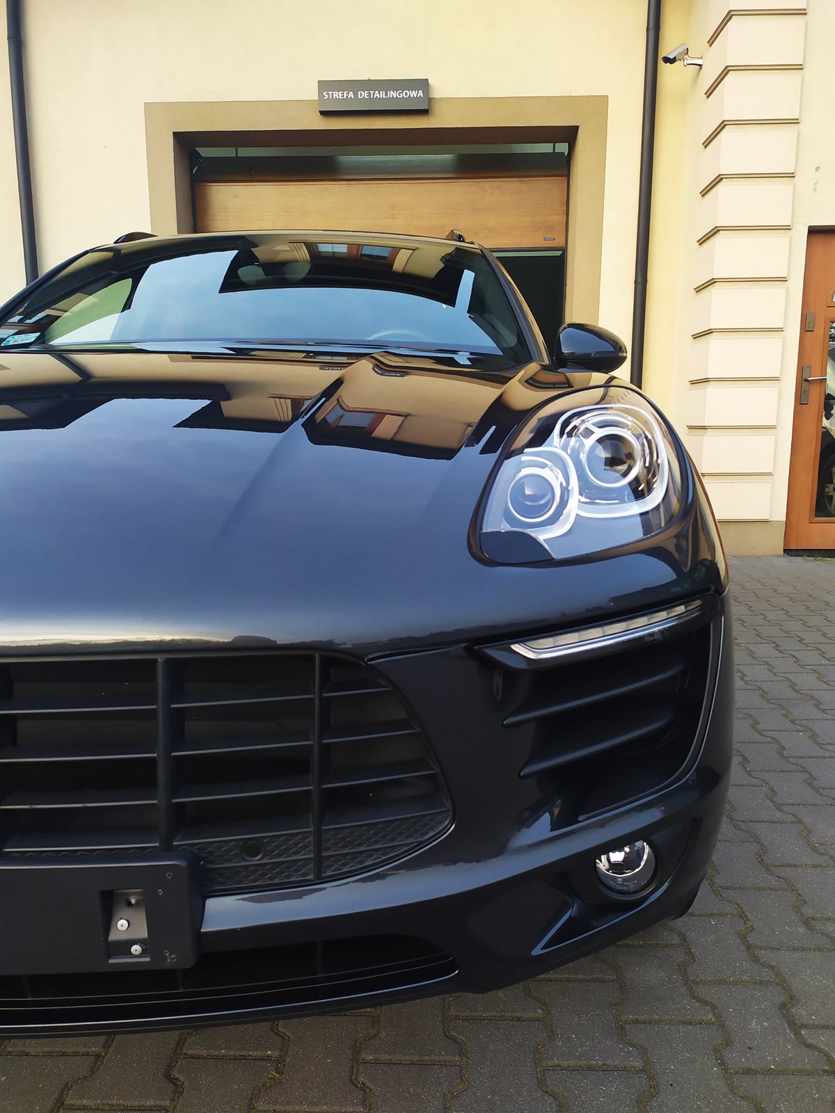 Grafitowe Porsche Macan z lustrzanym połyskiem przed bramą studia