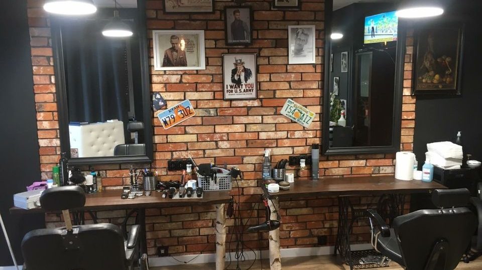 Wnętrze salonu: ceglana ściana, lustra i fotele barberskie